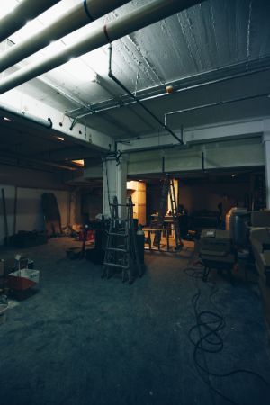 In a darkened storage room are ladders and a few objects. The back end of the room is lit by artificial light.