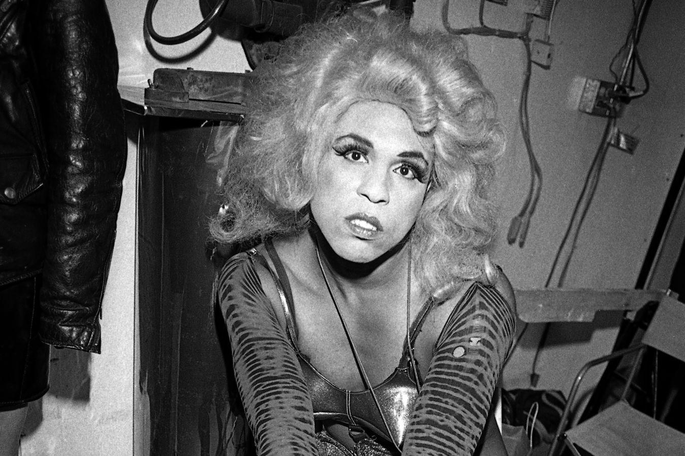 Eine Schwarz-Weiß-Portrait von Vaginal Davis mit blonder Perücke, die in die Kamera schaut.