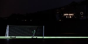 Ein Fußballtor auf einem Dunklen Spielfeld. Ein Leuchtschild zeigt BRD – DDR 