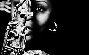 Black and white portrait of Matana Roberts, who can be seen out of focus behind a saxophone