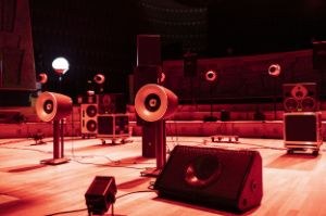 Various loudspeaker models stand on a stage and are illuminated in red.