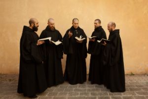 Five monks chant in a semicircle with books in their hands.