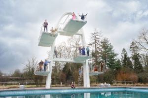 Eine Gruppe von Menschen steht auf den Plattformen eines Sprungturms im Freibad.