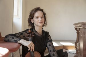 Eine junge Frau sitzt auf dem Boden und hat eine Violine in der rechten Hand.