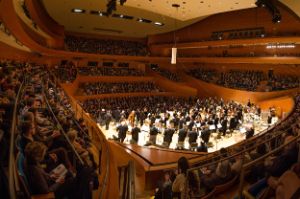The inside of a concert hall with lots of people and an orchestra in the centre