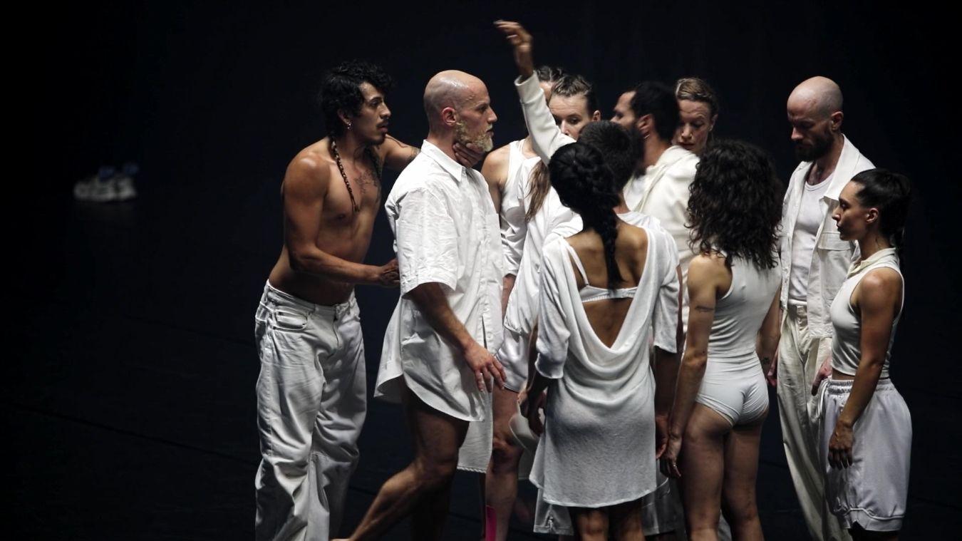 Ein Gruppe von Tänzer*innen in weißer Kleidung steht dicht gedrängt zusammen.
