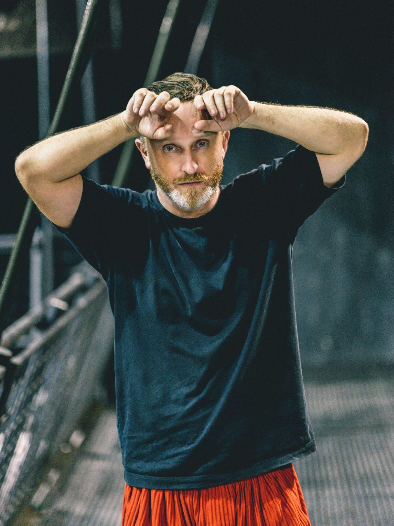 Damien Jalet greift sich mit beiden Handrücken an die Stirn. Er trägt legäre Kleidung und einen Vollbart.