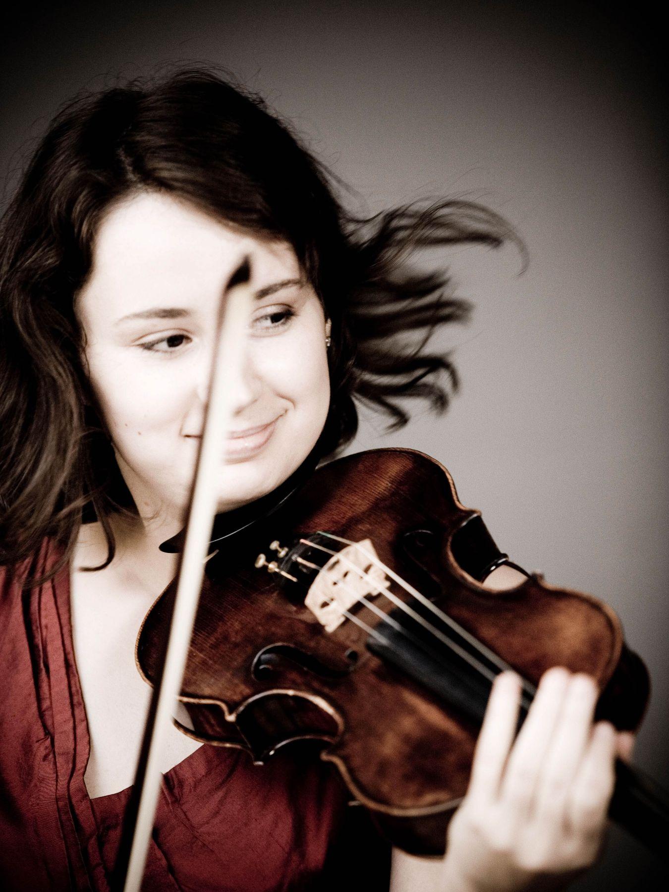 A woman plays the violin. Her hair is blowing.