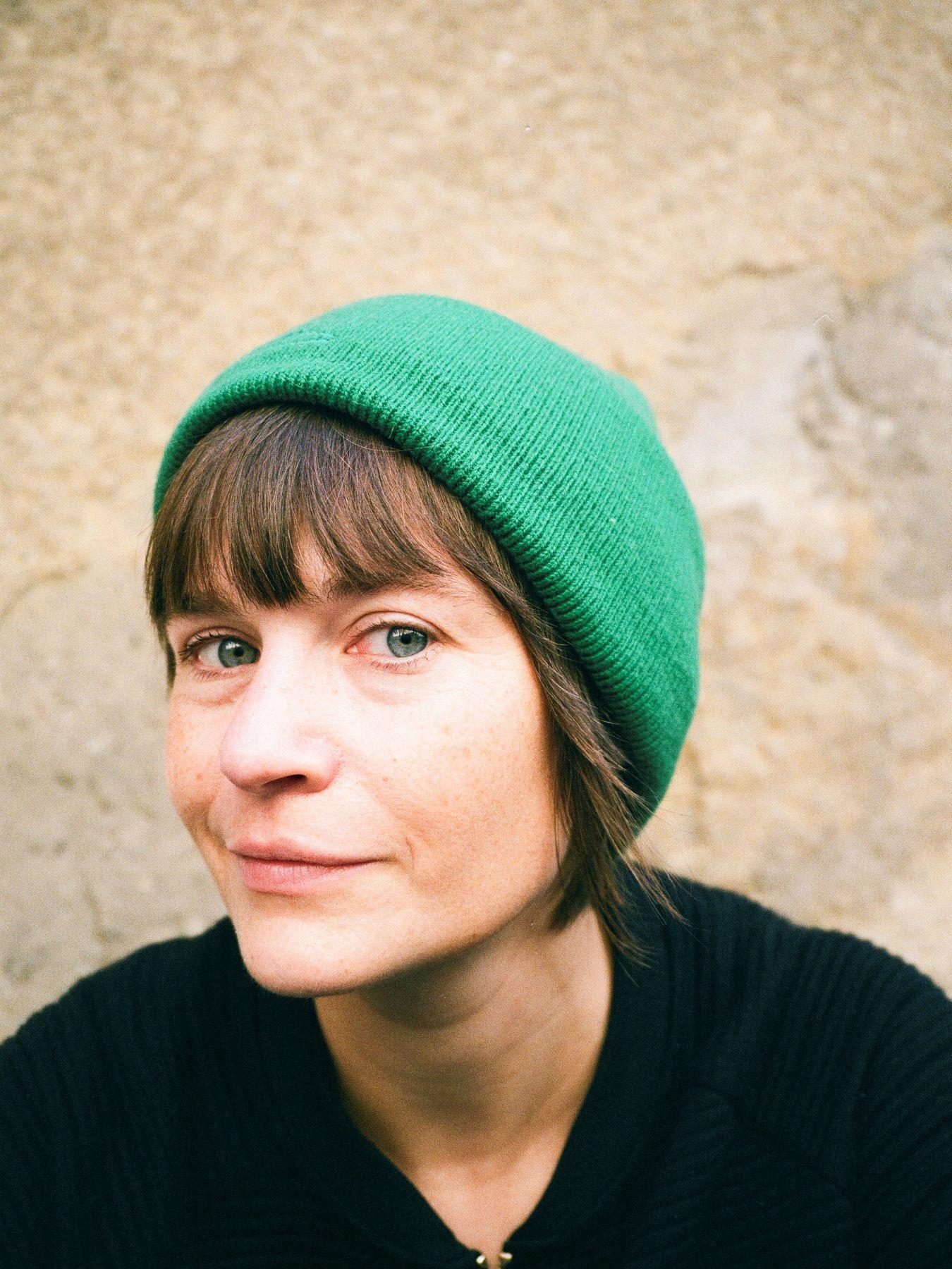 Eine Frau mit blauen Augen und einer grünen Mütze in einer schwarzen Weste.