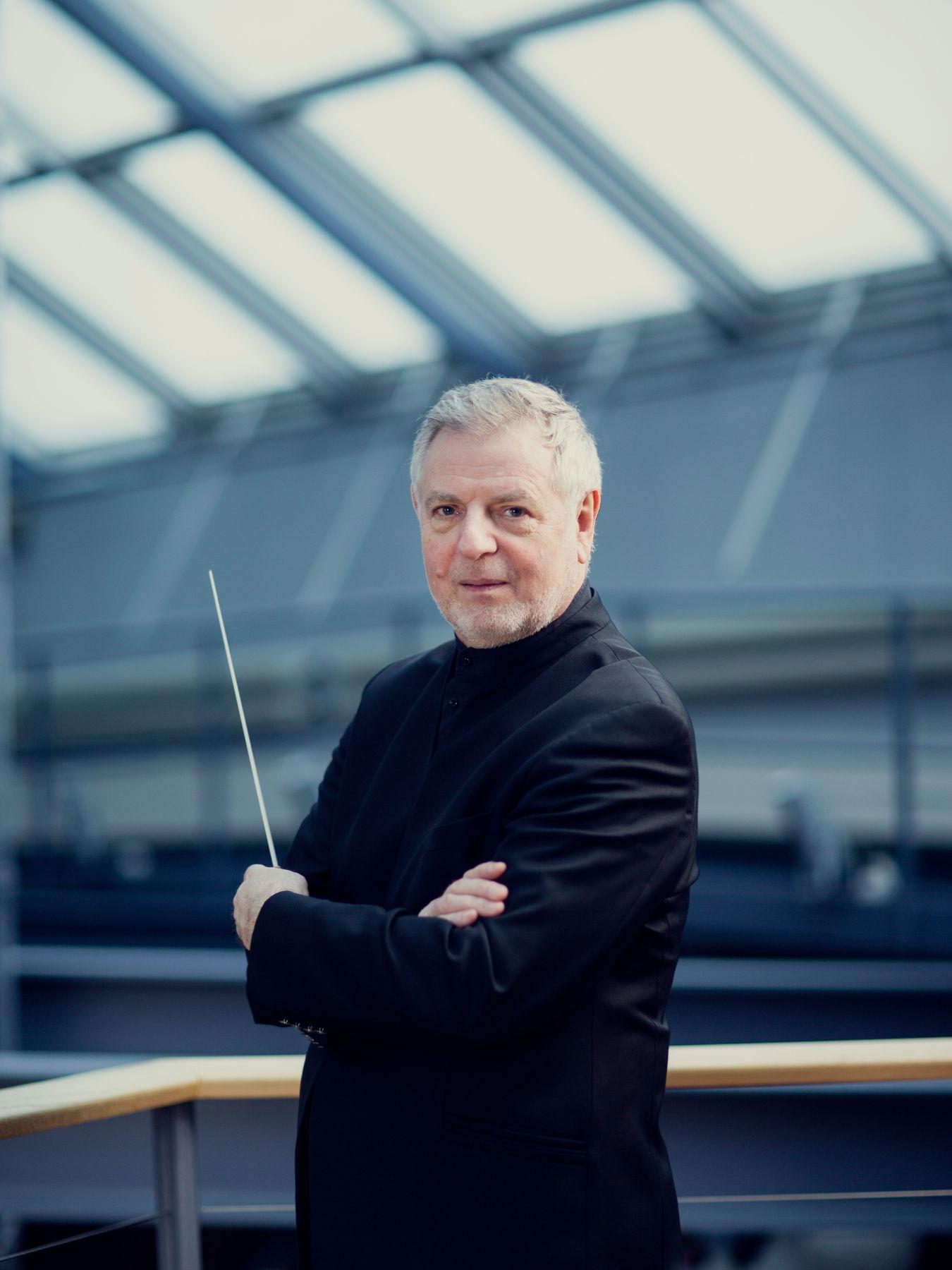 Steffens hat die Arme verschränkt und hält einen Dirigierstab.