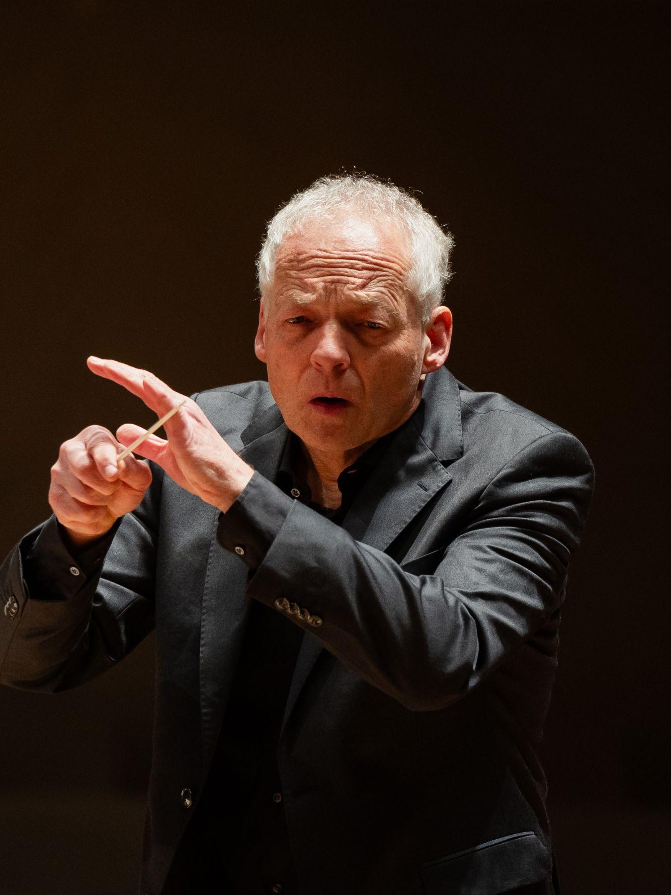 Matthias Hermann conducting, a man plays the violin in the background.