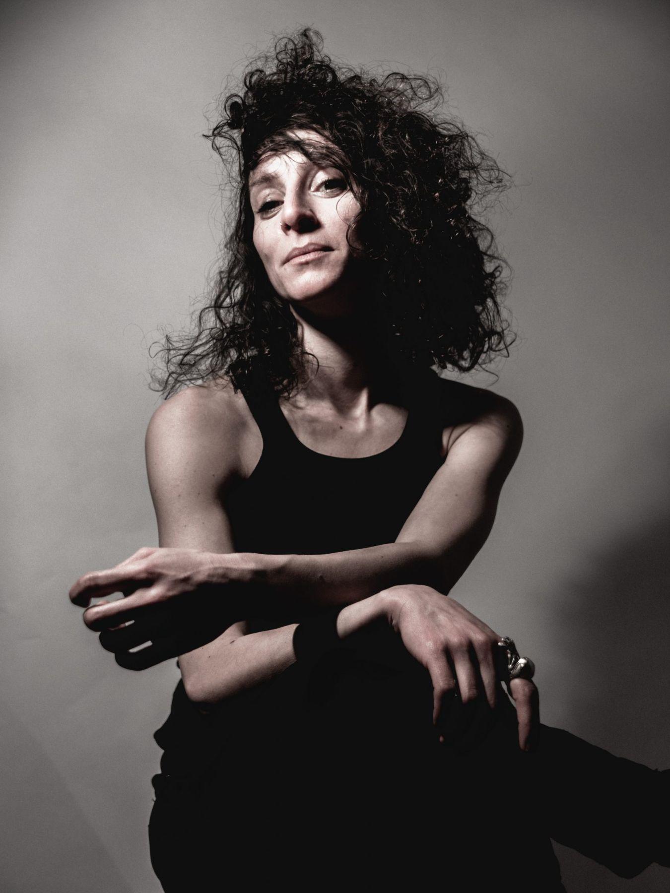 a female person with curly dark hair looks self-confidently into the camera