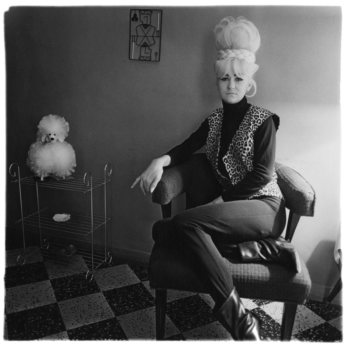 A person is sitting on a chair with her legs crossed. Next to the person is a shelf with an artificial souvenir dog on top.