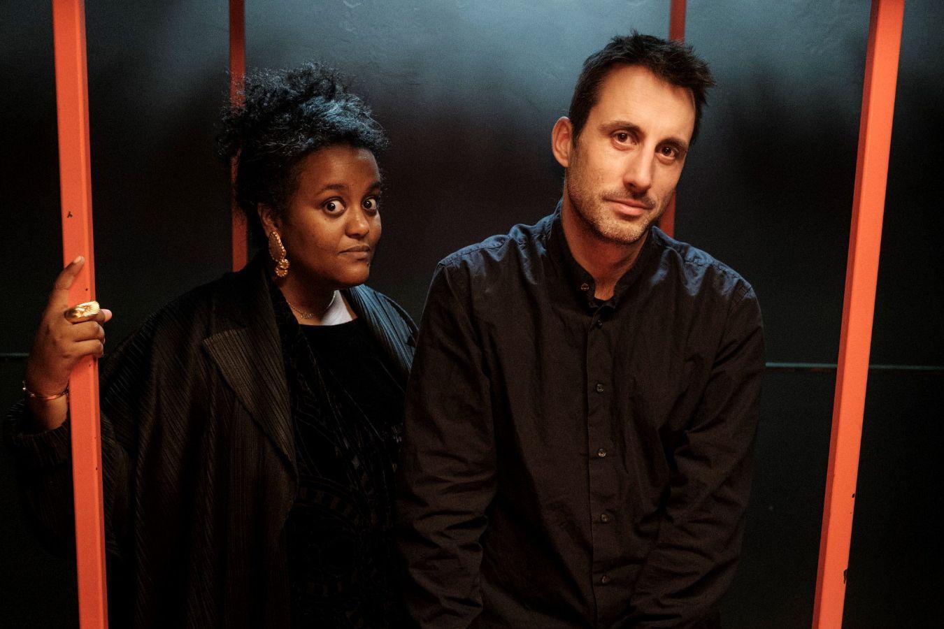 A man and a woman are standing between the orange coloured poles.