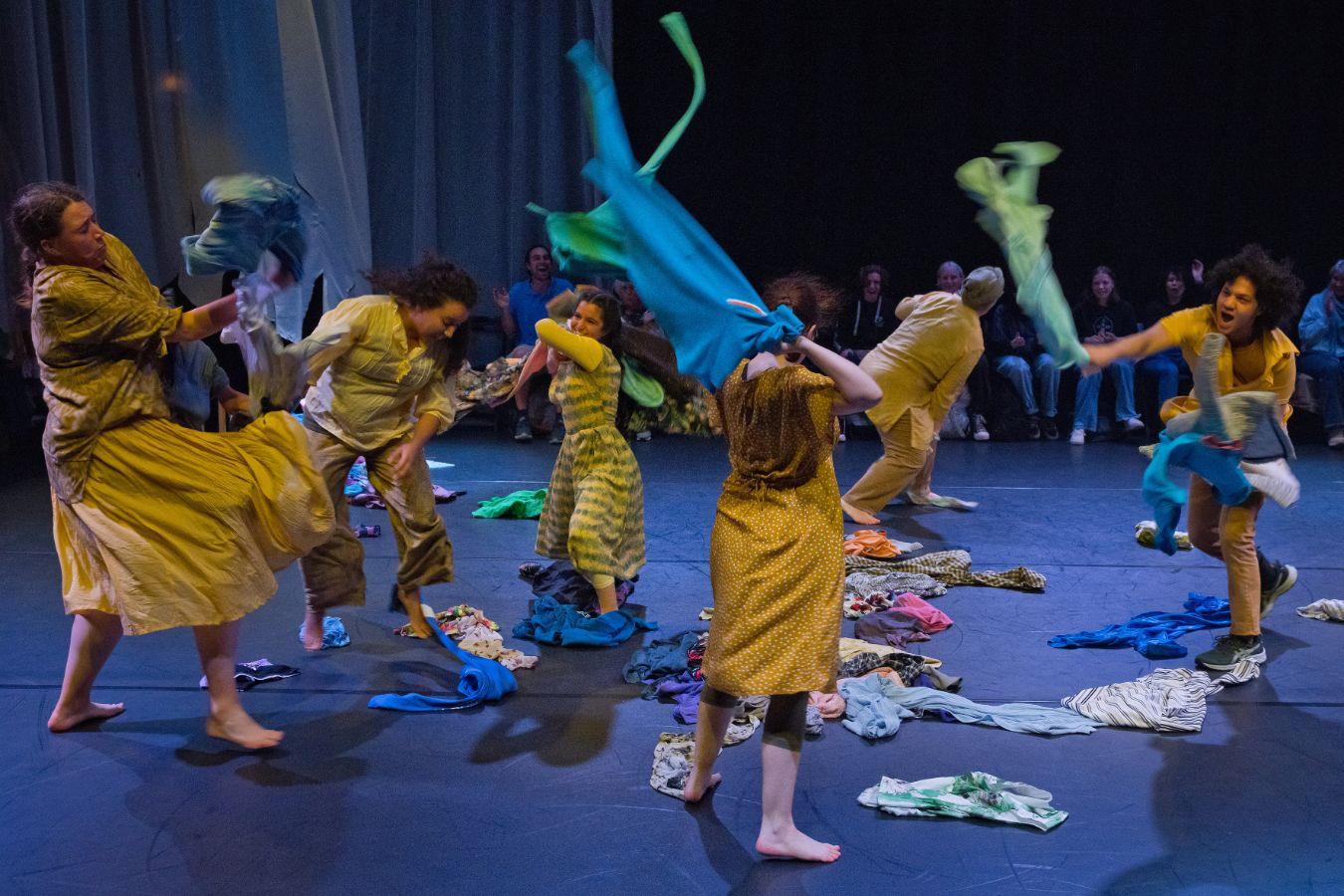 Six people are moving. They throw up clothes. Everyone is dressed in yellow. The stage is a circle and the audience sits around it.