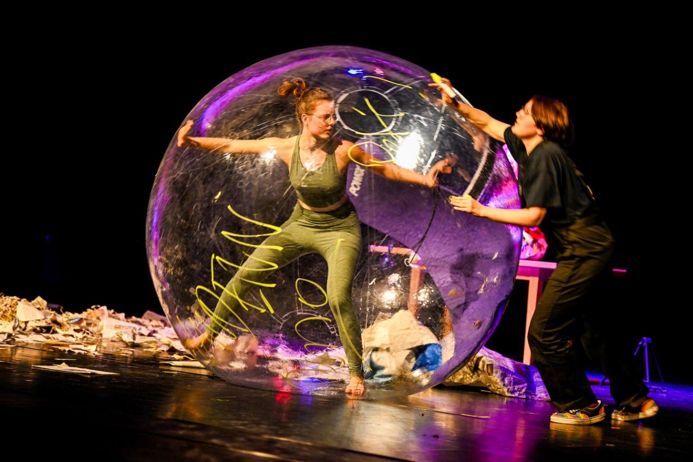 Eine junge Person steht in einer großen Blase, die eine andere Person stützt.