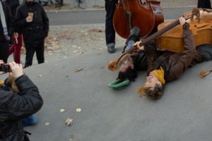 Joel Grip mit Kontrabass auf dem Bauch und Simon Sieger liegen auf dem Rücken auf Beton, im Vordergrund fotografiert eine Person die beiden.