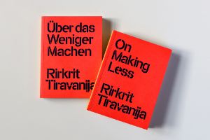 Zwei leuchtend rote Bücher liegen auf hellgrauem Hintergrund, auf ihnen steht in dunkelblauer Schrift gedruck "Über das Weniger machen. Rirkrit Tiravanija" und "On Making Less. Rirkrit Tiravanija".