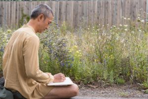 A man sits on the floor and draws plants.