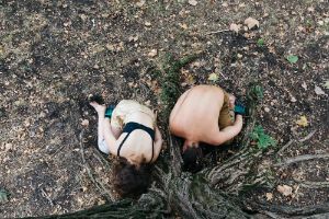 Two people nestle against the roots of a tree.