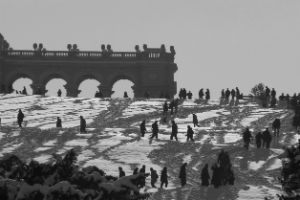 Menschen spazieren im Schnee einen Hügel hinauf, der von barocker Architektur bekrönt ist.