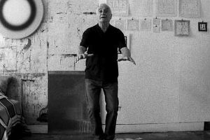 Film still from Rirkrit Tiravanija's "untitled 2008 (john giorno reads)", in which the artist John Giorno gestures towards the camera.