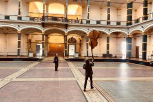 Eine Person balanciert einen Kontrabass auf einer Hand im Lichthof