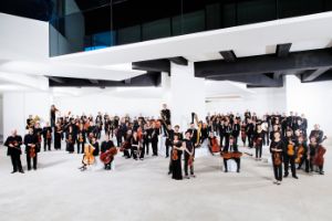 Musiker*innen eines großen Orchesters stehen mit ihren Instrumenten vor dem Konzertsaal.