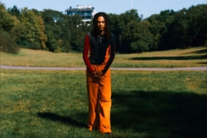 A photo of a person standing on a green meadow surrounded by trees.