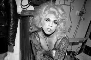 A black and white picture of Vaginal Davis with a blonde wig looking into the camera.