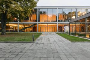 Grünfläche vor dem Haus der Berliner Festspiele, dessen Foyer ist hell ausgeleuchtet