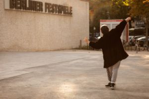 Eine Person von hinten gesehen tanzt mit ausgestreckten Armen vor einem Gebäude mit dem Schriftzug Berliner Festspiele.