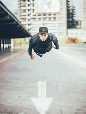 Portrait of a person in dark clothing. The person is hovering over a road, on the ground is an arrow pointing forwards.