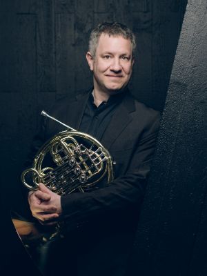 A man leans against a sloping wall with a horn