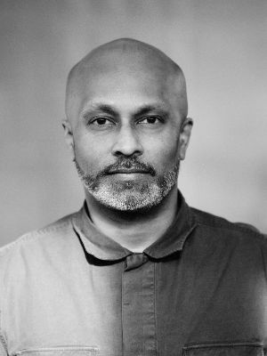 Black and white portrait: Akram Khan is bald and looks straight into the camera.