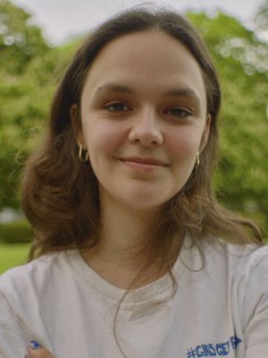 Ein Portrait einer Person im weißen T-Shirt, im Hintergrund Bäume