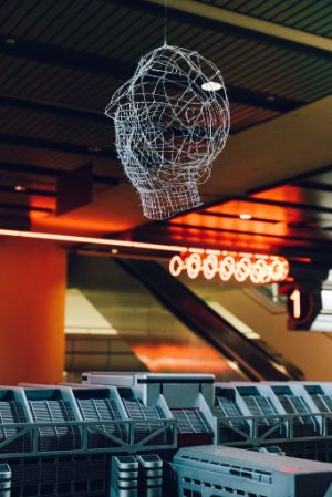 A delicate wire bust of a person. It hangs in the interior area of an orange-lit hall.