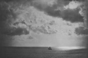 A wide sky full of clouds, below a ship sails on the sea.