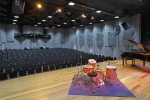 An auditorium with a stage on which there is a grand piano and a drum kit