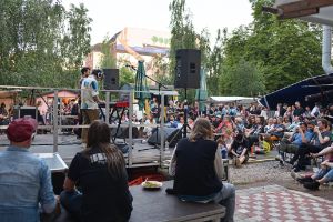 Two musicians play on an open-air stage in front of an audience sitting in deckchairs.