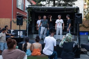 Four actors on a small open-air stage, audience on benches in front of it