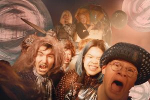 The ensemble of the piece pulls a covered wagon towards the viewer. Shiny metallic spheres reflecting the surroundings float in the background.