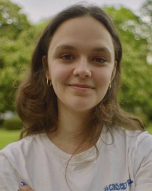 A portrait of a person in a white T-shirt, trees in the background