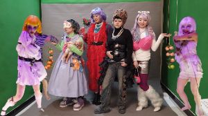 Six people in colourful costumes stand in front of a silver photo background.