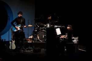 Three people play piano, electric guitar and drums