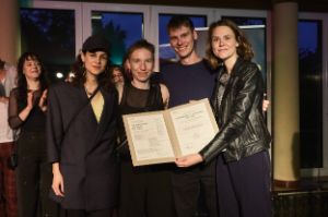 The artistic team of “ÜBERGEWICHT, unwichtig: UNFORM” holds the Theatertreffen certificate in front of the audience.