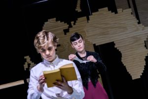 Two young women in old-fashioned costumes are each reading a book. One woman is in the foreground of the picture and out of focus. The second woman is further in the background and is clearly recognisable.