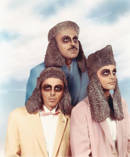 3 persons with dark make-up around the eyes, who wear caps with long earflaps